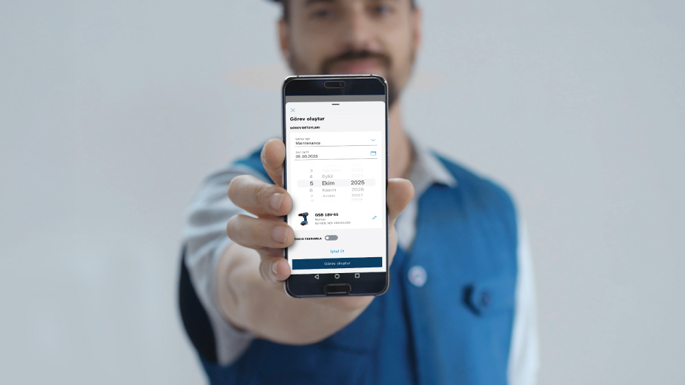 一个男人展示了一部智能手机，上面有一个显示任务细节的应用程序。他穿着一件蓝色衬衫。