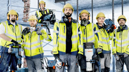 六名戴着黄色安全帽和警示背心的建筑工人在工地上站着。