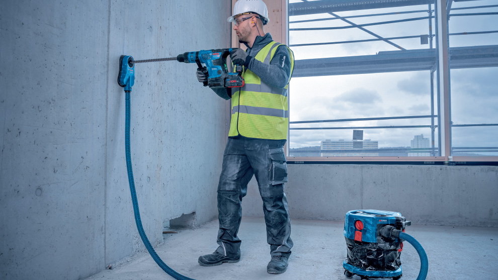 一个戴着头盔和背心的男人正在钻一个混凝土墙。