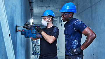 两个戴着安全帽的男人操作一台博世专业机器。