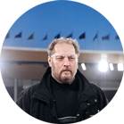 一个留着胡子的男人穿着黑色夹克，站在聚光灯下。