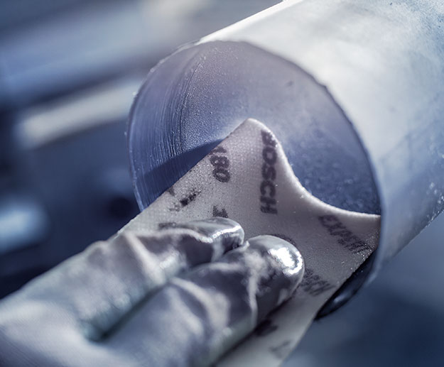 一只手握着博世砂纸在一个圆形金属件上。